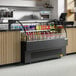 An Avantco black horizontal air curtain merchandiser on a counter with drinks and snacks in it.