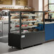 An Avantco black refrigerated bakery display case with cakes on display.
