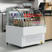 An Avantco white horizontal air curtain merchandiser with drinks on a shelf inside.