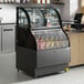 An Avantco black refrigerated display case with a curved glass door and dual service shelves holding drinks.