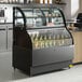 An Avantco black curved refrigerated air curtain merchandiser on a counter with bottles of liquid in it.