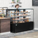 A woman standing behind a black Avantco dry bakery display case with pastries on glass shelves.