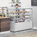 A woman behind a 72" Avantco refrigerated bakery display case filled with cakes.