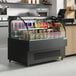 An Avantco black horizontal air curtain merchandiser with drinks and snacks inside.