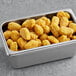 A metal container filled with Queso Loaded Tots.