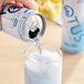 A hand pouring Lotus Plant Power Blue Lotus Energy Drink from a can into a glass of ice.