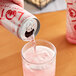 A hand pouring Lotus Plant Power Red Energy Drink into a glass of pink liquid with ice.