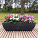 A Floridis Amsterdam rectangular black planter with pink and white flowers on a table on an outdoor patio.