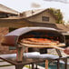 A man using the Ooni Koda 2 Max to cook a pizza on a table in an outdoor patio.