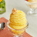 A glass bowl of yellow ice cream with a cookie on top.