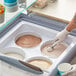 A hand in a white glove scooping white ice cream from a white HDPE tub.