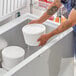 A man putting a white LDPE ice cream tub cover on a white ice cream tub.