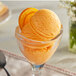 A glass with orange ice cream in it on a table.