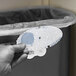 A gloved hand placing a Fresh Products Curve Mango Scent air freshener in a trash can.
