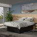 A Rize Home black steel platform bed base with wood panels in a room with a bed and painting on the wall.