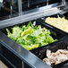 A Vollrath black polycarbonate food pan with chicken, lettuce, and eggs on a buffet counter.