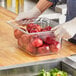 A person wearing gloves using a Vollrath 6" deep clear polycarbonate food pan on a counter with a plastic container of red apples.