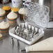 A white container with Ateco pastry bags and nozzles inside on a counter with cupcakes.