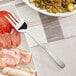 A plate of meat and vegetables with an American Metalcraft stainless steel cold meat fork on it.