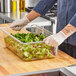 A person in gloves using a Vollrath clear polycarbonate food pan to serve salad at a salad bar.