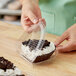 A person putting a brown and white cookie in a Polar Pak clear plastic hinged container.