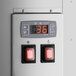 A grey digital control panel with a digital display and red buttons.