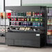 An Avantco black extra deep vertical open air merchandiser with drinks and snacks displayed in it.
