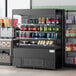 An Avantco black vertical open air merchandiser with drinks and snacks on display.