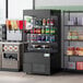 An Avantco black vertical open air merchandiser with drinks and snacks on shelves.