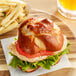 A sandwich on a Ditsch soft pretzel bun with fries on a wooden plate.