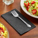 A fork on a Hoffmaster black paper napkin next to a plate of salad.