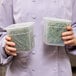 A woman holding two Cambro translucent square polypropylene containers of herbs.