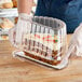 A person in gloves holding a cake in a Polar Pak clear plastic half cake container with dome lid.