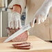 A person in white gloves using a Choice Classic carving knife to cut meat on a wooden cutting board.