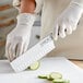 A person in white gloves using a Choice Classic Nakiri Knife to slice a cucumber on a cutting board.