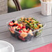 A clear plastic Sabert two-compartment bowl with fruit and salad in it.