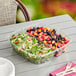 Sabert clear plastic two-compartment bowl set filled with fruit and vegetable salad on a table.