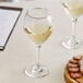 A plate of food and two Acopa Bouquet wine glasses filled with white wine on a table.