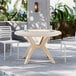 A Grosfillex Ibiza sandstone round pedestal table with chairs and an umbrella by a pool.