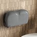 A grey Lavex Pro stone double-roll jumbo toilet paper dispenser on a tile wall.