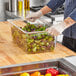 A person in gloves using a Vollrath clear plastic food pan to hold lettuce at a salad bar.