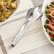 A bowl of salad with American Metalcraft hammered stainless steel serving tongs on a table.