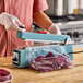 A person using a Galaxy 8-inch impulse heat bag sealer with a cutter and timer to seal a plastic bag containing food.