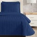 A bed made with a Berkshire Hospitality twin size blue quilt with a botanical leaf pattern.