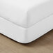 A white woven faux linen box spring cover on a white bed frame.