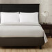 A Berkshire Hospitality King Size Gray Mist Pucker Jacquard top sheet on a bed with a black headboard and white pillows.