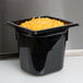 A Vollrath black polycarbonate food pan containing cheese on a counter.