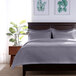 A bed with a Berkshire Hospitality gray diamond quilted bedspread and a lamp with a plant.