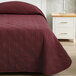 A bed with a Berkshire Hospitality CozyCare burgundy bedspread on it.