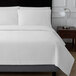 A Berkshire Hospitality white Ogee matelasse coverlet on a bed with white sheets.